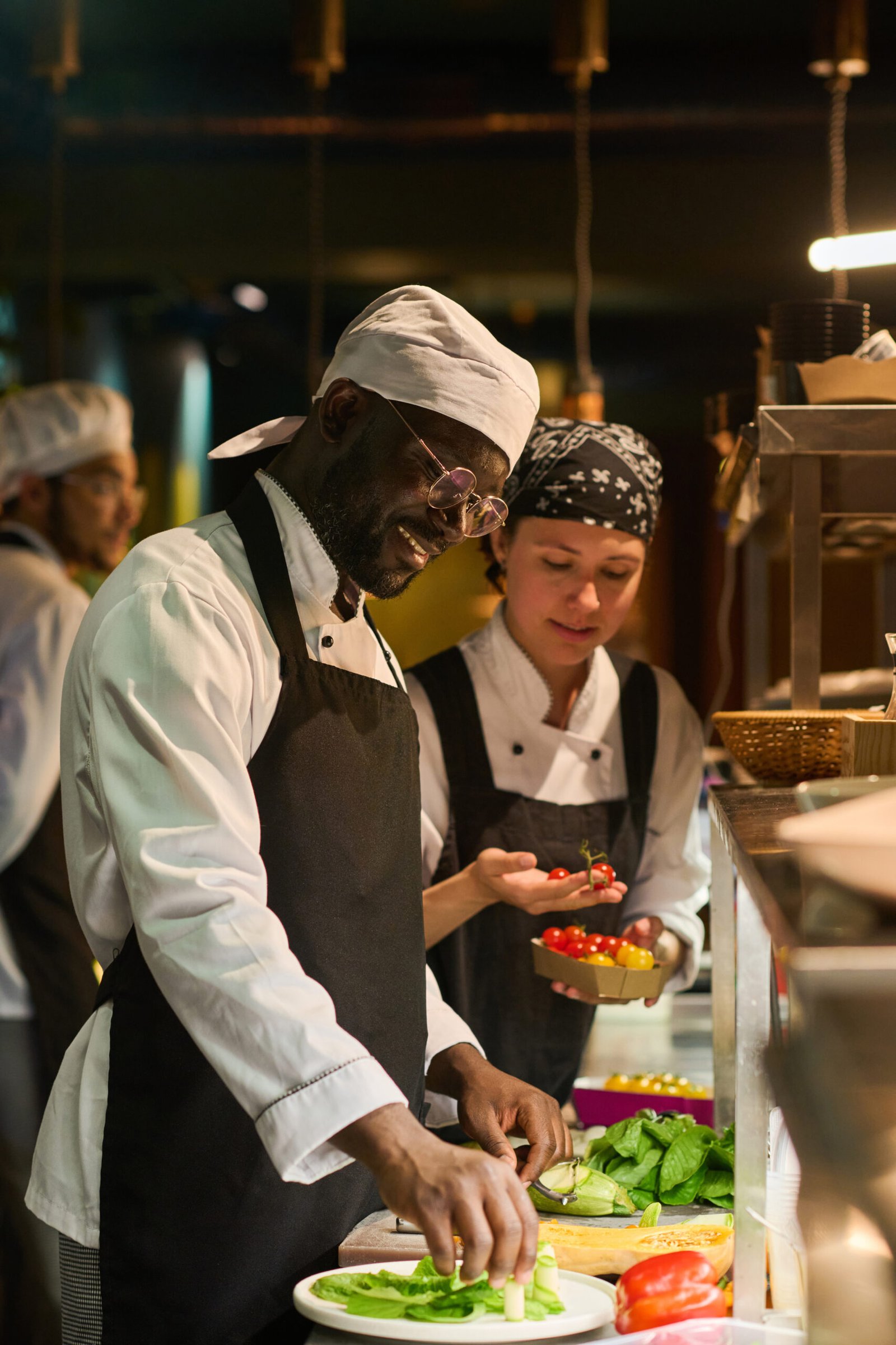 Happy young African American male chef mixing fresh ingrdients on board Happy young African American male chef in uniform mixing fresh ingredients on small round board before putting it into pan