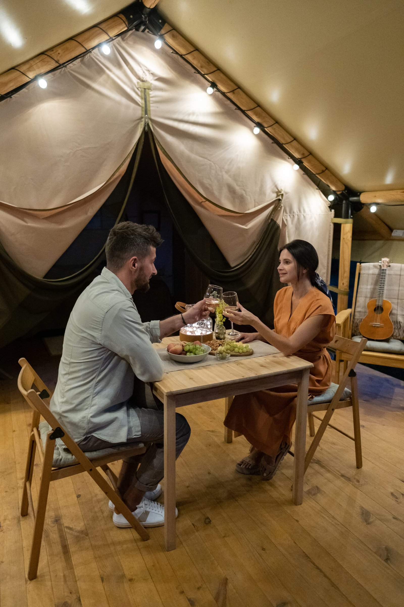 Young amorous couple cheering up with glasses of wine by romantic dinner Young amorous couple cheering up with glasses of wine over served table on patio of glamping house